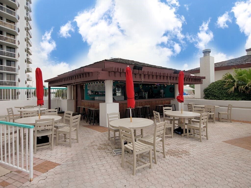 An outdoor patio with round tables and chairs, a covered seating area, and a view of a high-rise building.