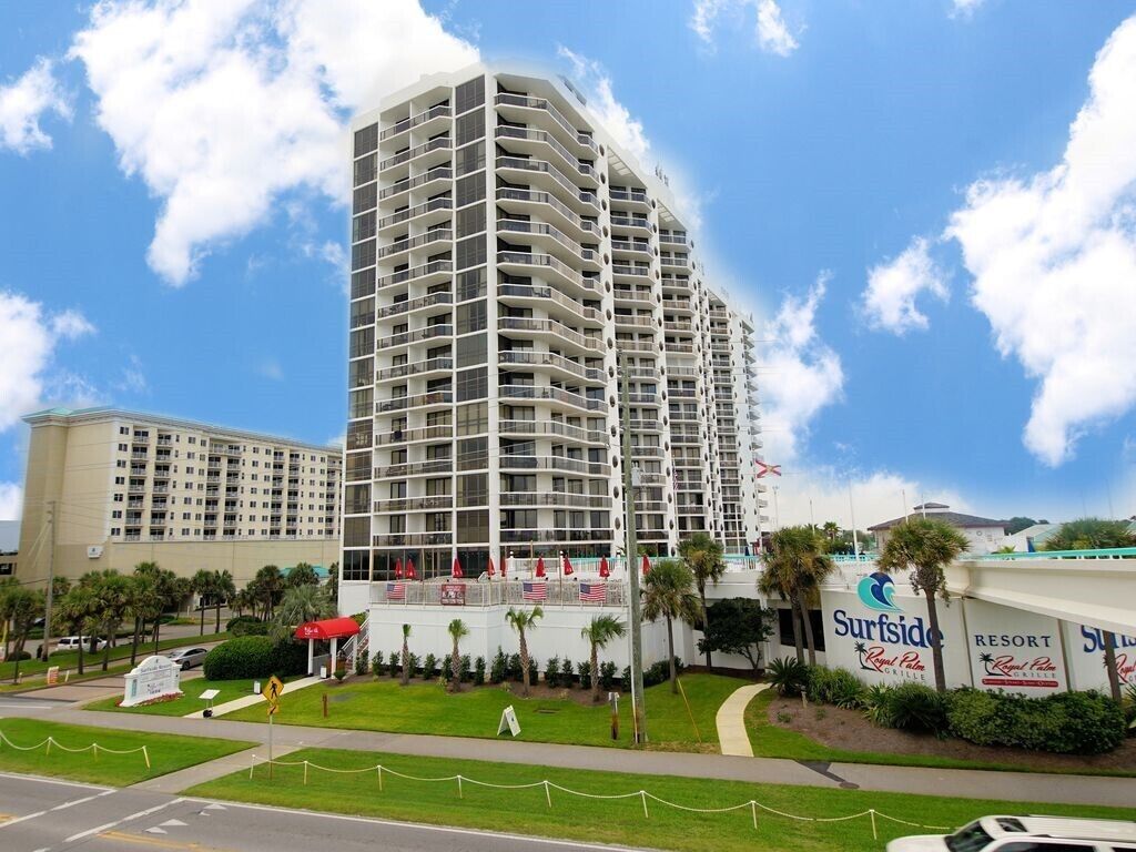 A high-rise hotel with multiple balconies, a swimming pool area, and a resort sign.