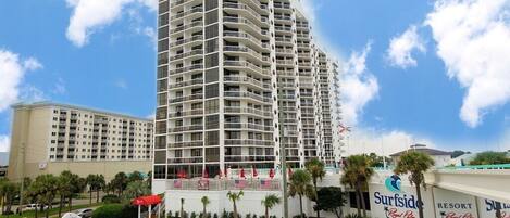 A high-rise hotel with multiple balconies, a swimming pool area, and a resort sign.