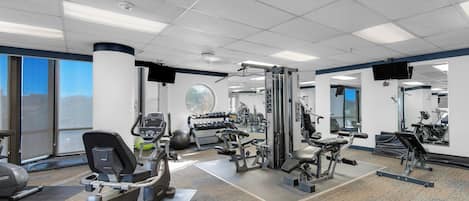 Un gimnasio con máquinas de cardio, equipo de levantamiento de pesas y espejos.