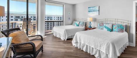 A hotel room with two beds, a balcony with a view of the city, wicker furniture, and a large window.