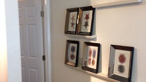 Een gang met een witte deur, een houten stoel en een wandplank met ingelijste foto's.