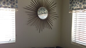 Een kamer met een donkerblauwe bank, een decoratieve spiegel met een zonvormig omlijsting en raam gordijnen met een patroon.