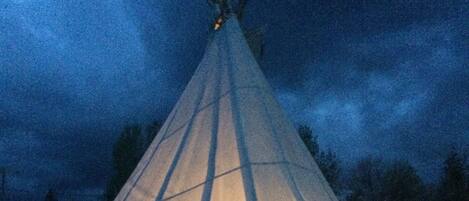 A tipi with a triangular shape and a conical roof, illuminated from within.