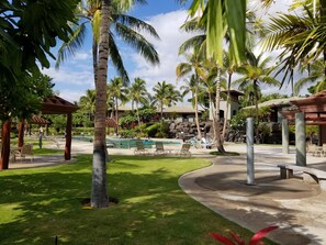 Et resortområde med swimmingpool, palmer, liggestole og en pavillon.