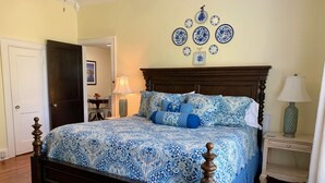 A bedroom with a wooden bed, a nightstand, a lamp, and a wall-mounted plate decoration. - Bear House 1890, Johnson Retreat, Mins from Downtown, Perfect Luxurious Getaway! (Chattanooga)