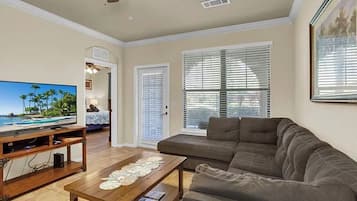 A living room with a television, sofa, coffee table, ceiling fan, and large windows.