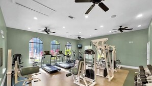 Ein Fitnessstudio mit Laufbändern, Kraftgeräten und einem Deckenventilator.