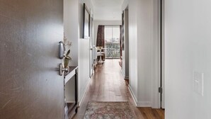 A hallway with a wooden floor, a patterned rug, a ceiling light fixture, and a door with a number.