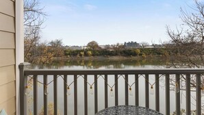 A covered outdoor area with a metal table and chairs, overlooking a body of water and distant buildings.