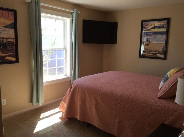 A bedroom with a bed, a window with curtains, a flat-screen TV mounted on the wall, and two framed pictures. - Beautiful Family Home, Wifi, 5 Minute Walk To The Beach. (Pacific City)