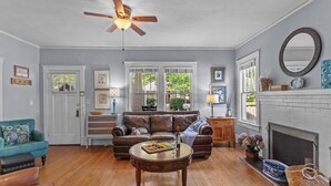 A living room with a sofa, a coffee table, a ceiling fan, a fireplace, and a window with a view of greenery.