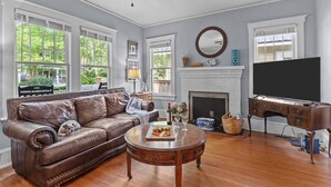A living room with a leather sofa, a coffee table, a fireplace, a TV, and large windows.