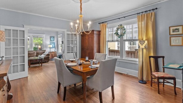 A dining room with a wooden table, chairs, a chandelier, and a view of the outdoors.