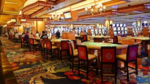 Un casino doté de nombreuses tables de jeu et de chaises, d’un tapis à motifs et de décorations ornementales au plafond.