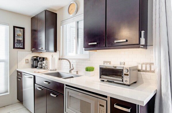A modern kitchen with dark cabinets, a white countertop, a toaster, and a coffee maker.
