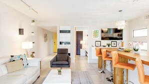 A modern living room with a sofa, coffee table, and a dining area with bar stools. - Modern Palm Springs Retreat • Resort Pool + Hot Tub • Quiet & Central Location (Palm Springs)