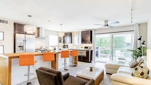 A modern kitchen with a central island, bar stools, and a dining area with a sofa and coffee table. - Modern Palm Springs Retreat • Resort Pool + Hot Tub • Quiet & Central Location (Palm Springs)