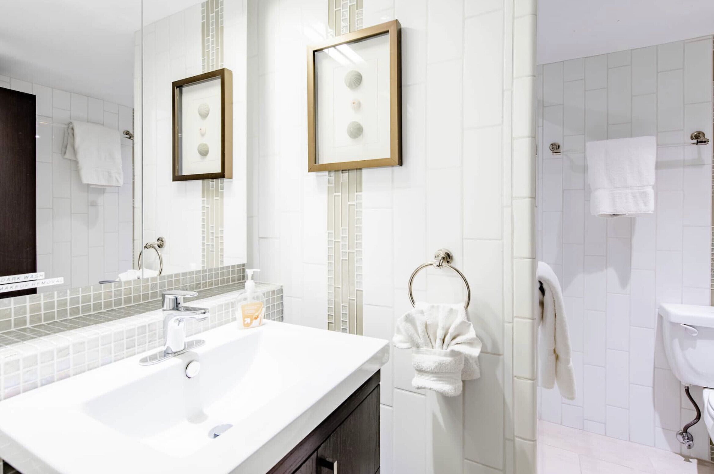 A modern bathroom with a white sink, two framed mirrors, and a toilet.