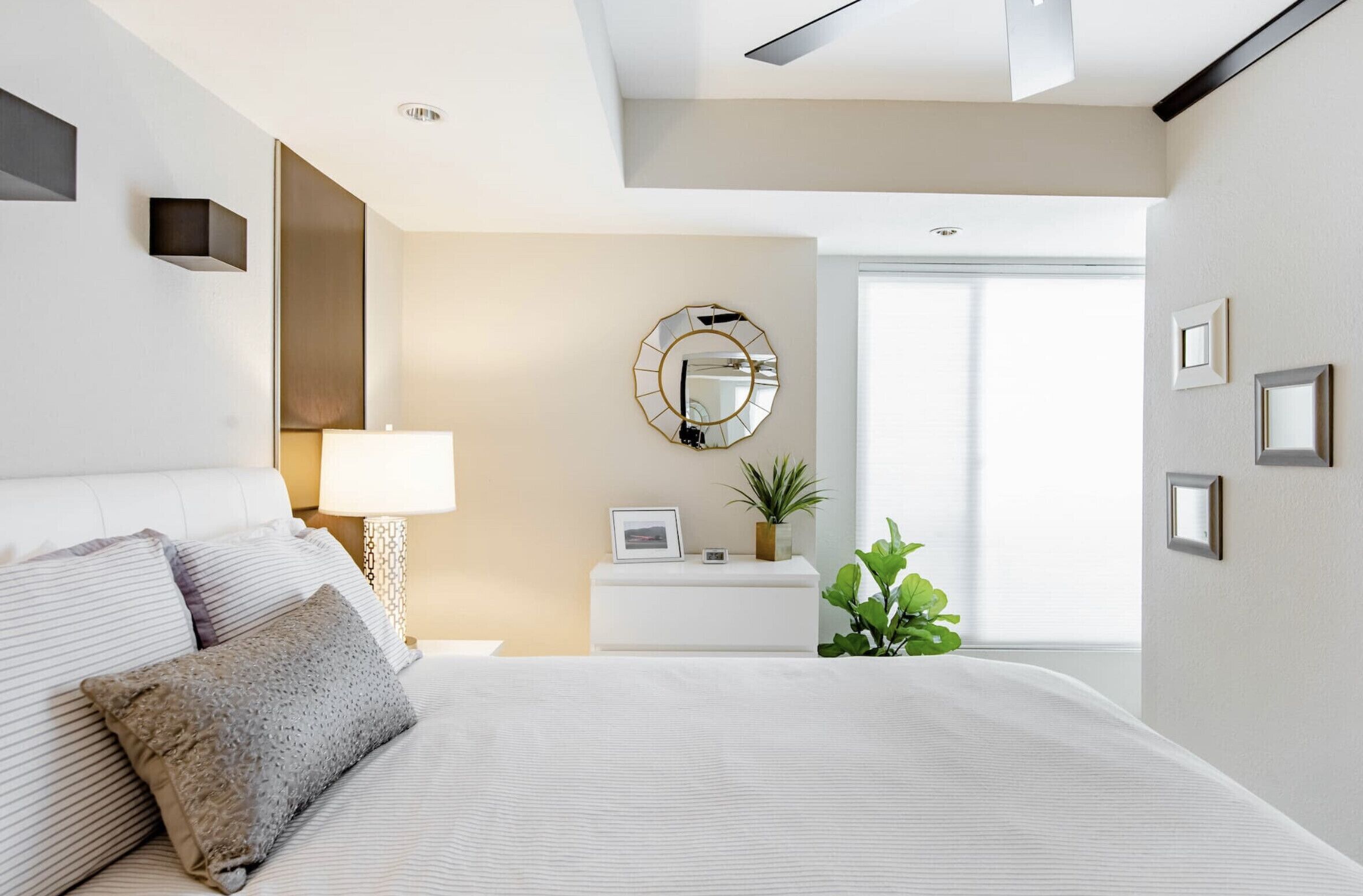 A modern bedroom with a large bed, bedside table, lamp, and a mirror on the wall.