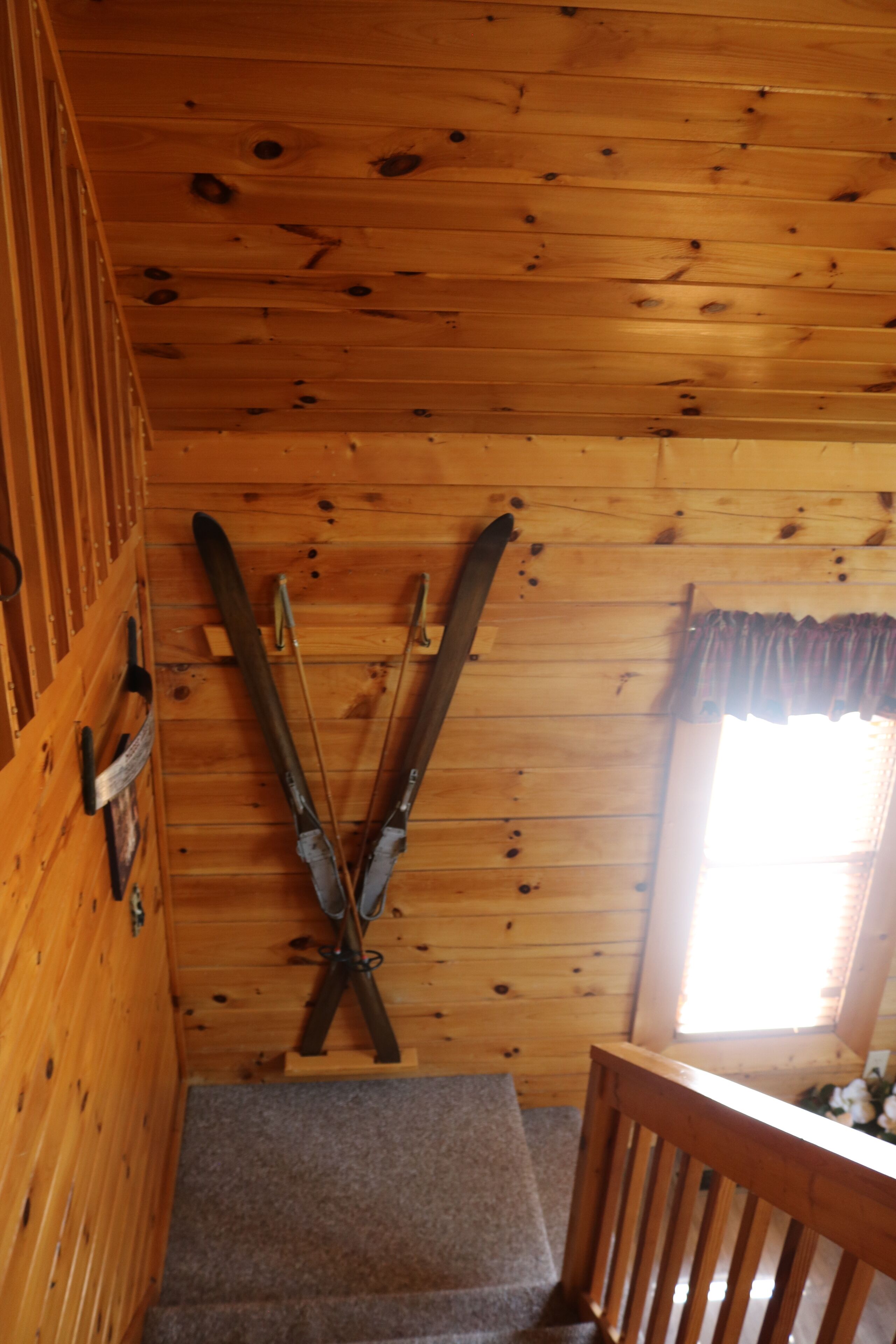 A wooden cabin interior with a pair of skis leaning against the wall and a window with curtains.