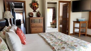 Een slaapkamer met een bed, een dressoir, een spiegel, een televisie en een deur naar een andere kamer.