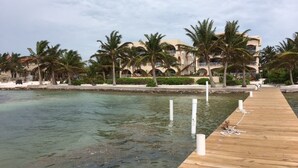 Een houten steiger die leidt naar een strandhotel met palmbomen en helder water.