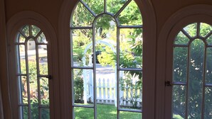 Ein Zimmer mit drei Rundbogenfenstern, die auf einen Garten mit weißem Zaun und viel Grün blicken.