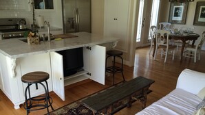 Eine moderne Küche mit einer großen Kochinsel, ein Essbereich mit einem Holztisch und Stühlen sowie ein gemütliches Wohnzimmer mit einer Couch und einer Bank.