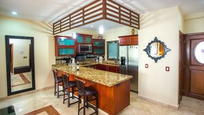 A kitchen with a central island, bar stools, a refrigerator, and a microwave. - Spacious, quiet and safe condo one block from the beach in Playacar (Playa del Carmen)