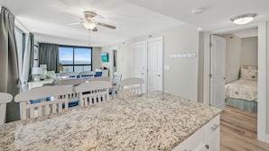 A modern kitchen with granite countertops, white cabinetry, and a dining area with white chairs.