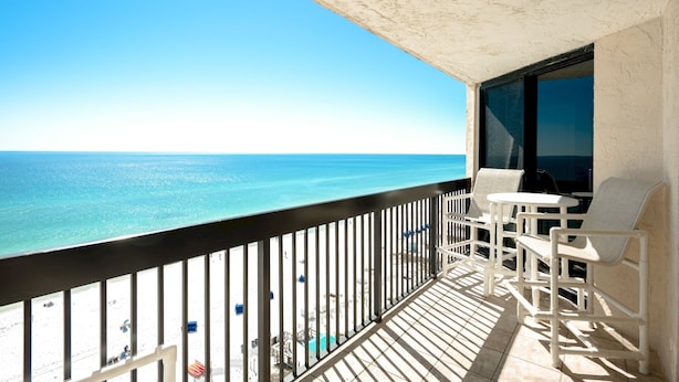 A balcony with a view of the ocean, white chairs, and a table.