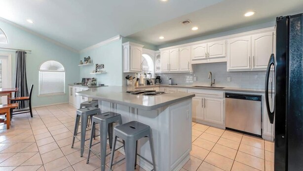 A spacious kitchen with a large island, white cabinetry, and a black refrigerator. - 2300 sq ft Beach close, spacious 5 star townhome, garage and parking! (South Padre Island)