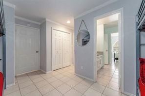 A hallway with a white door, a mirror, and a view into a room with a bed and a window.