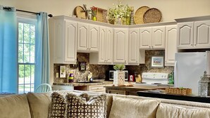 A modern kitchen with white cabinets, a built-in stove, and a dining area with a beige sofa and patterned cushions. - Your Creekside Villa Experience: Relax and Refresh. Brookhill Ranch Area!  (Hot Springs Village)