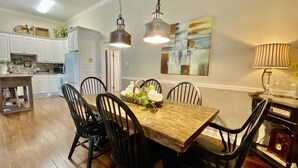 A dining area with a wooden table and black chairs, a kitchen in the background, and a painting on the wall. - Your Creekside Villa Experience: Relax and Refresh. Brookhill Ranch Area!  (Hot Springs Village)