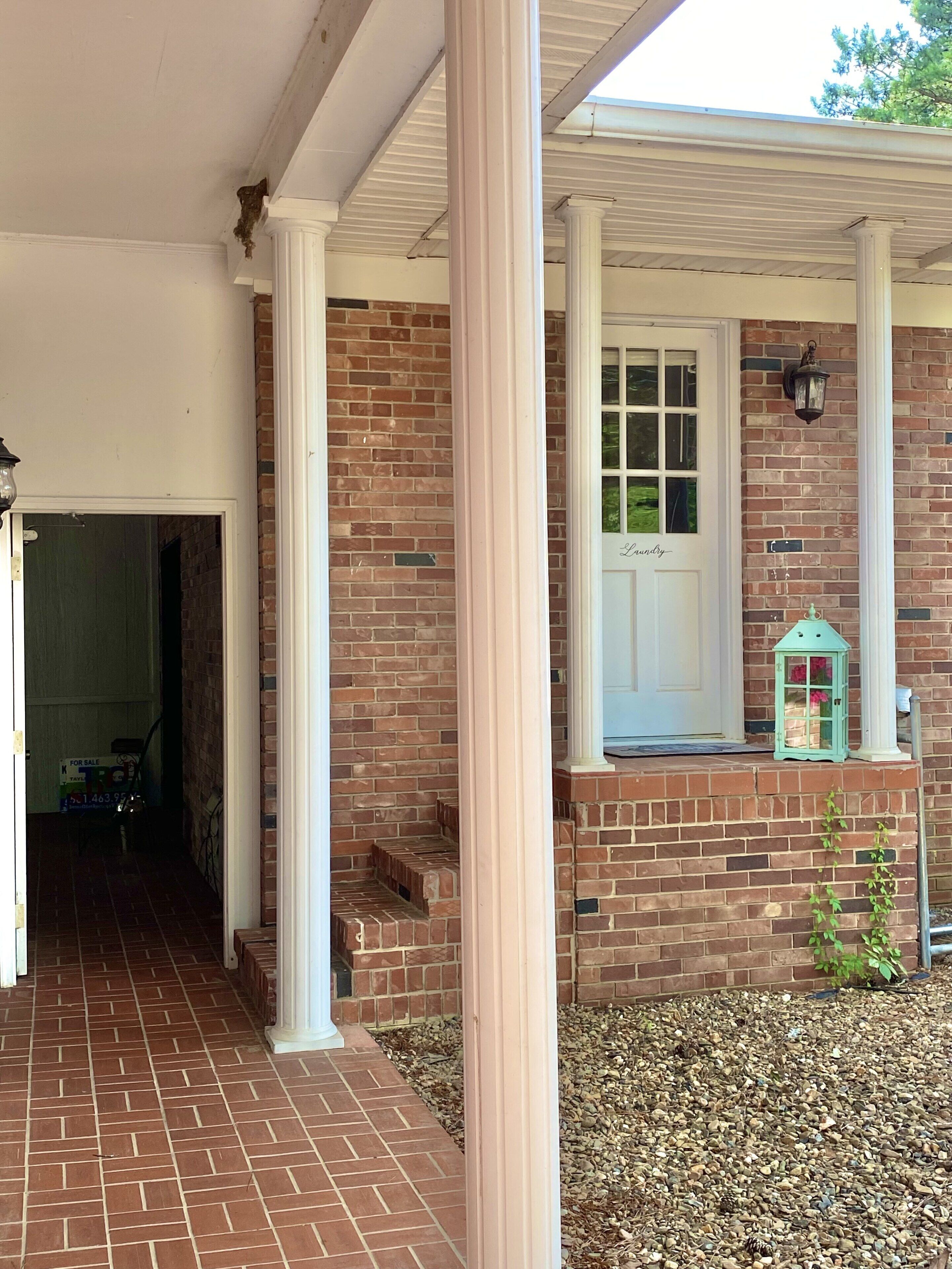 A brick exterior with a white door and columns, a small porch area with a lantern, and a gravel driveway.