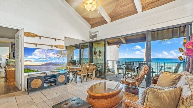 A spacious living area with a large TV, comfortable seating, and a view of the ocean.