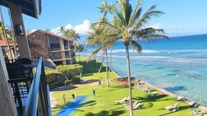A view of a hotel balcony overlooking a pool area with palm trees and a clear view of the ocean.