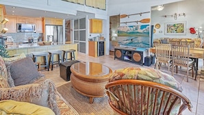 A spacious living area with a high ceiling, a kitchen with modern appliances, and a dining area with wooden furniture.