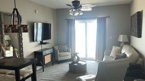 Un salon équipé d’un téléviseur, d’un ventilateur de plafond, d’un canapé, d’une table basse et d’un coin repas avec une table et des chaises.