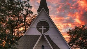 A church with a red door and a cross on the steeple, surrounded by trees. - Walk to the Beach and Downtown Restaurants, Bars, and Shops! (Ocean Springs)