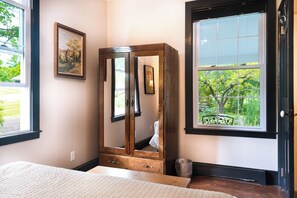 A bedroom with a large mirror, a bed, a window with a view of greenery, and a framed picture on the wall. - Late summer on the Wine Trail is the best! Everything is happening now. (Burdett)