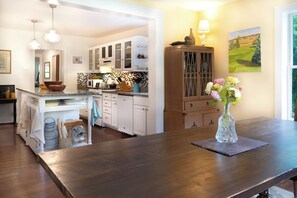 Una cocina con armarios blancos, una mesa de comedor de madera y un jarrón con flores.