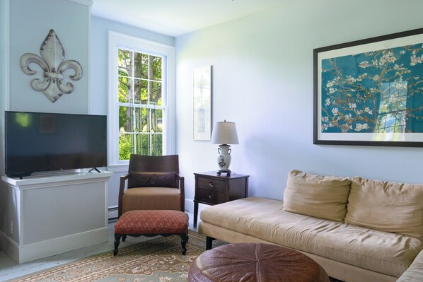 A living room with a television, a chair, a sofa, a rug, and a painting on the wall.