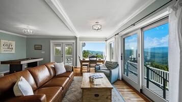 A spacious living room with a leather sofa, a wooden coffee table, and a view of a balcony with a scenic landscape.