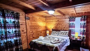 Ein gemütliches Schlafzimmer in einer Blockhütte, mit einem Bett, einem Nachttisch und einem Fenster mit Vorhängen.