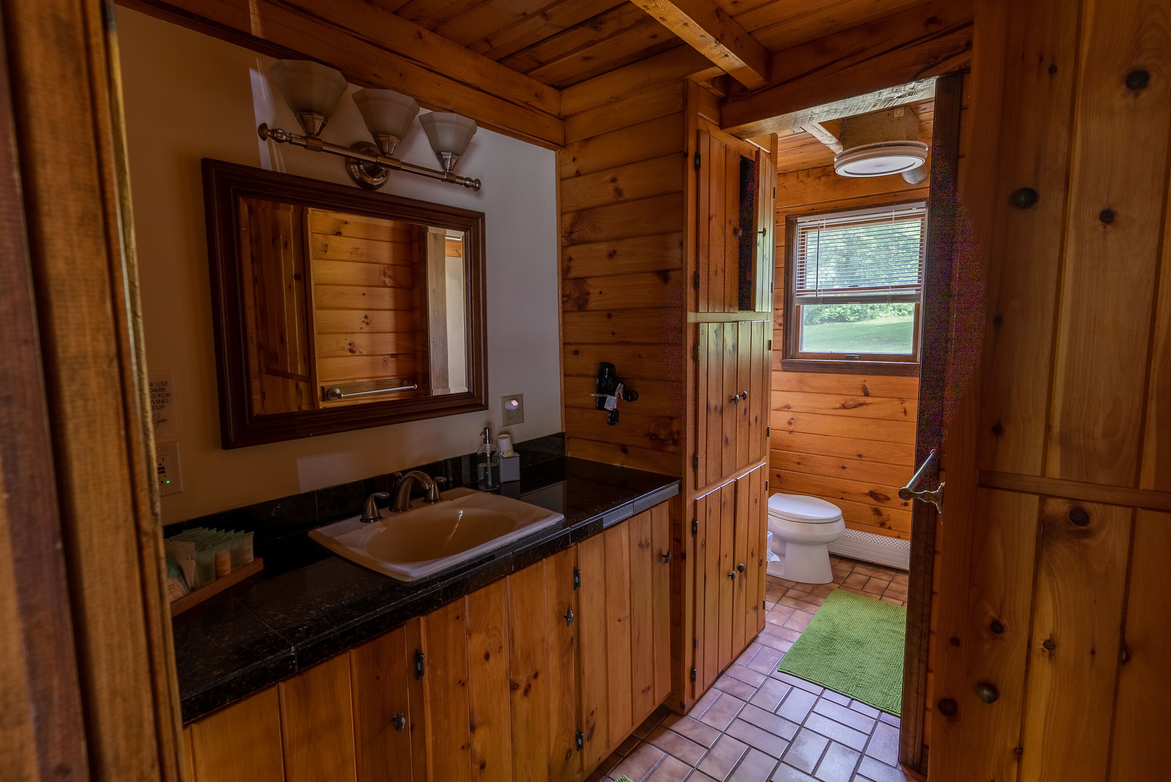 Ein Badezimmer einer Holzhütte mit Waschbecken, Spiegel und Toilette.