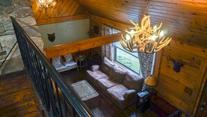 Ein gemütliches Blockhaus-Interieur mit einer Holztreppe, einer gepolsterten Sitzecke, einer Kristallleuchtre und einer Steinwand.