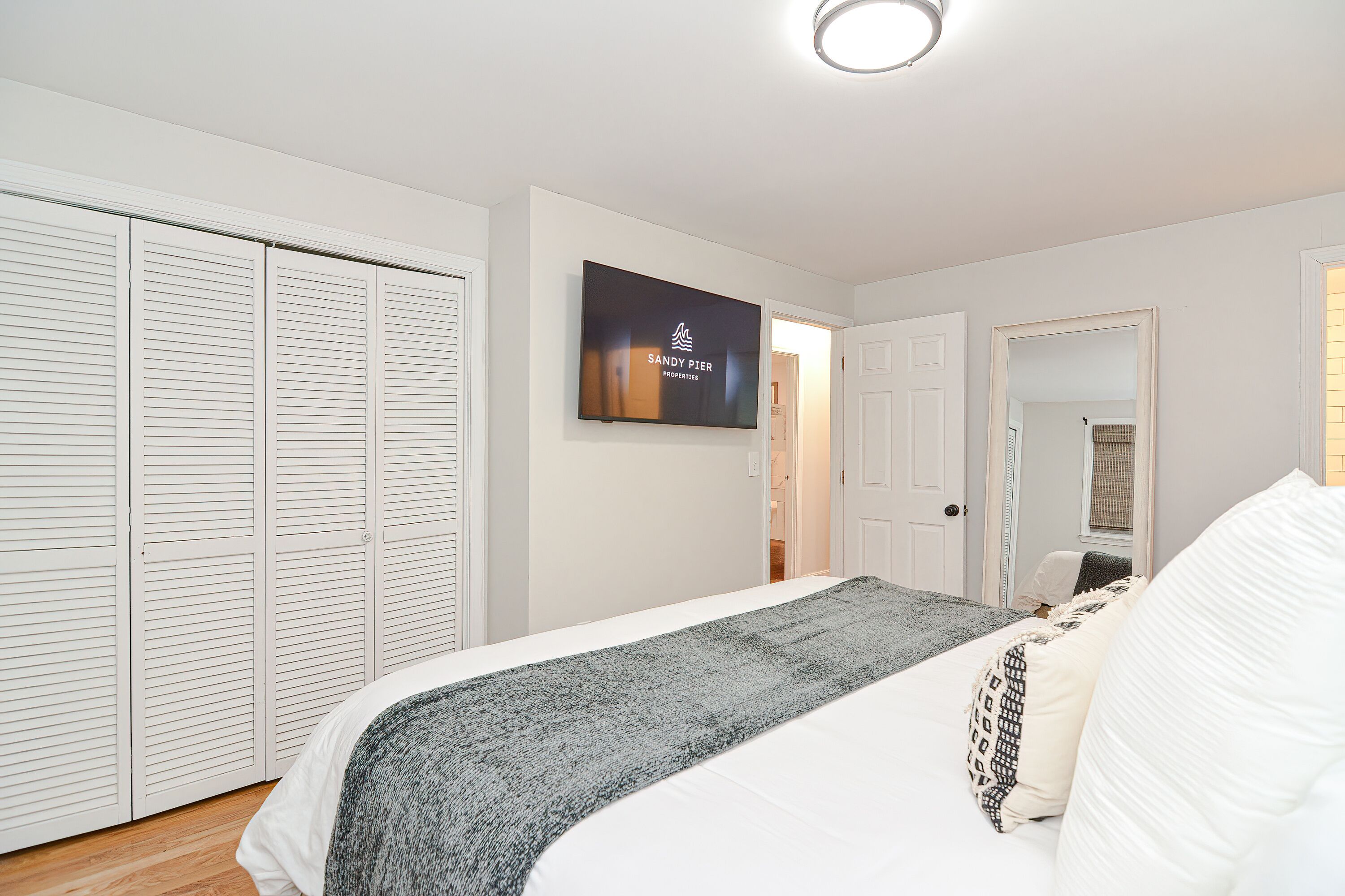 Un dormitorio con cama, televisor, armario y puerta que da a otra habitación.